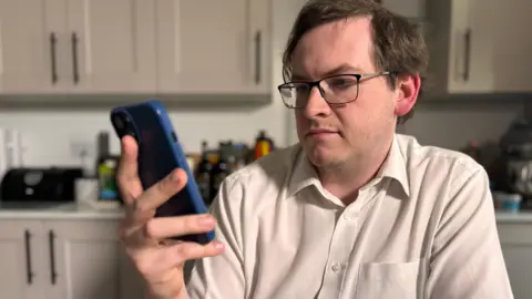 Patient Matthew Rainbow is looking at his phone which he used to book the DocSelect appointment through an app