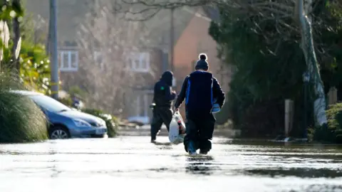 PA Media A person walking through floodwater