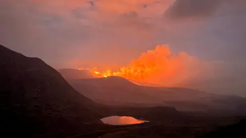 Orange smoke rising from the top of a mountain. 