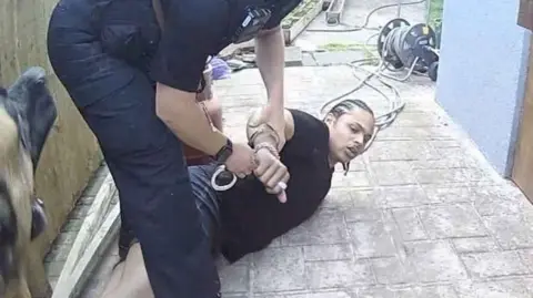 Nottinghamshire Police Bodycam still of an arrest being made on a patio, with a police dog barking