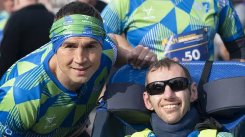 Kevin Sinfield (left) and Rob Burrow (right). Both are wearing green and blue patterned shirt. Sinfield has a bandana on his head and Burrow is wearing black sunglasses.