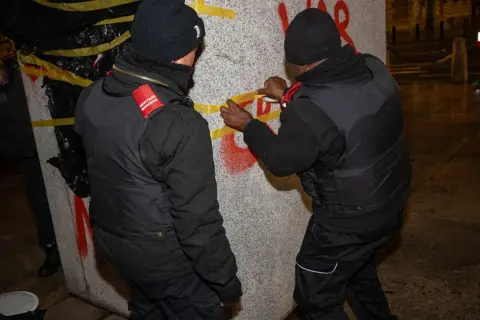 Getty Images Two men dressed in black cleaning the statue's plinth