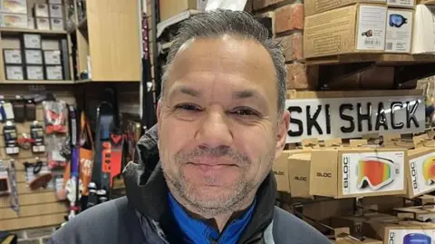 Shop manager John Ali next to a sign which reads 'Ski Shack'