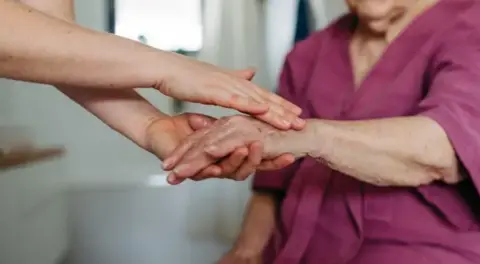 Getty Images A file image of a carer reaching out to hold the hand of an older person