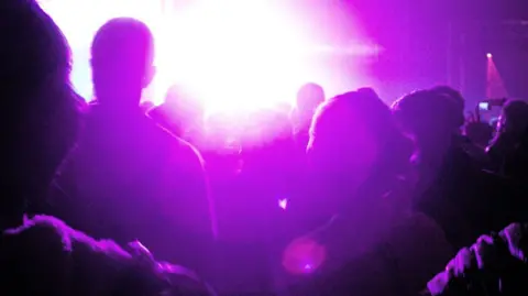 Unidentifiable dancers at a rave bathed in pink light