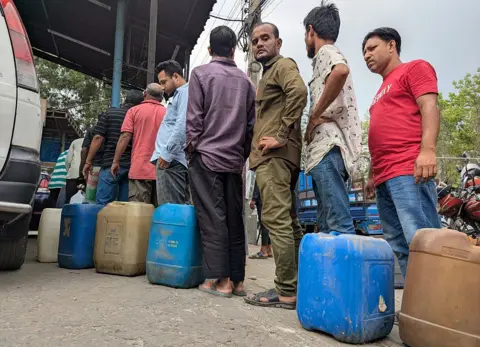 NurPhoto via Getty Images Motorists wait in line to purchase fuel at a petrol station in the Mohammadpur area of Dhaka, Bangladesh, amid concerns over global oil supply disruptions linked to escalating tensions in the Middle East. 