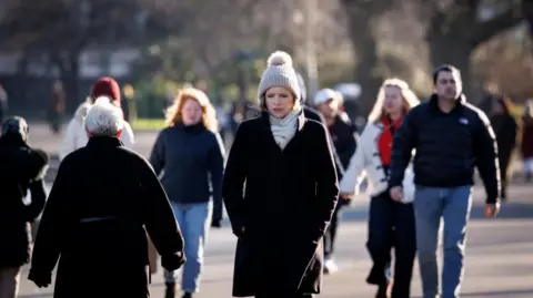 A woman walking amongst a crowd of people through Regent's Park in London on 3 January 2025. She is wearing a grey pom-pom hat and scarf, with a black coat