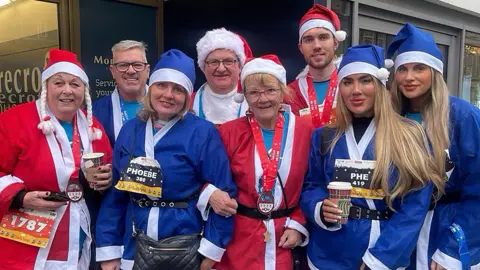 A group of eight people, dressed up in red and blue Santa costumes, looking at the camera and smiling. 