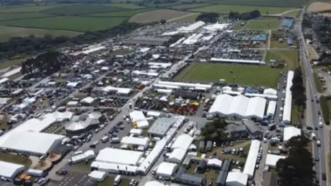 An aerial view of the Royal Cornwall Showground in Wadebridge in 2024. There are lots of white marquees and tents around the site, with cars and people dotted around as well.