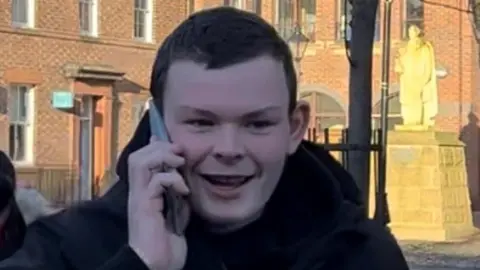 Brian Harold is walking outside Carlisle Crown Court. He has short black hair and is talking on the phone.