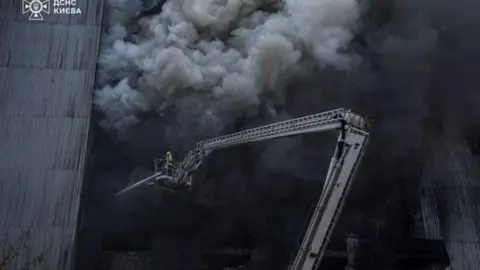 DSNS Ukraine A firefighter puts out a smoky fire at a large grey warehouse