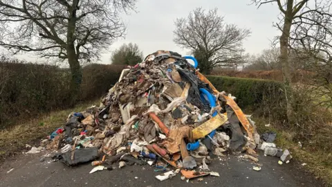 BBC A huge pile of illegally dumped waste material which appears to include housebuilding materials and tubing and various other items.