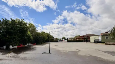 Ant Saddington/BBC A large expanse of tarmac at a primary school. There are trees on the left, two netball hoops in the middle of the playground and single storey buildings on the far right. 