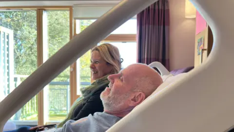 BBC/NATHAN TURVEY Nikki Smith and Darren Powell lying on the cuddle bed at St Leonard's Hospice in York smiling.