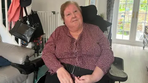 Irene Harvey sitting in a wheelchair in her house