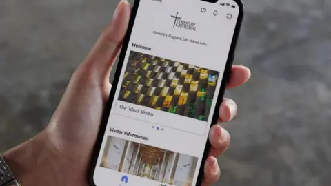 A phone with the new app open in the palm of someone's hand. The person is wearing a silver watch. 