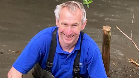 Iain Wheller in a blue polo shirt standing in a river