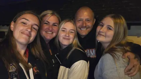 Family handout A family selfie with three teenage girls with long hair, an older woman and man. It is taken at night and they are all standing close together and smiling at the camera.