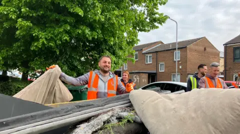 A group of men in high visibility tops throwing rubbish into a skip