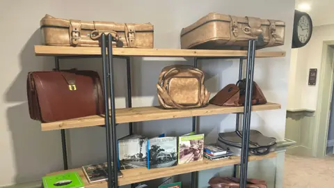 Amy Holmes/BBC A collection of old bags, suitcases and books on shelves.