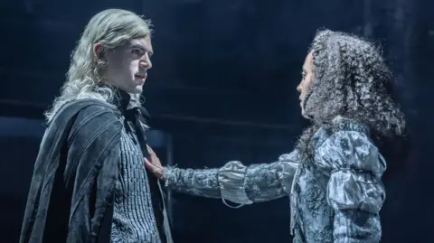 Noah Ritter (Prince Rhaegar Targaryen) and Harmony Rose-Bremner (Lyanna Stark) facing each other in costume in a scene from Game of Thrones: The Mad King. She has an arm outstretched with her palm on his chest