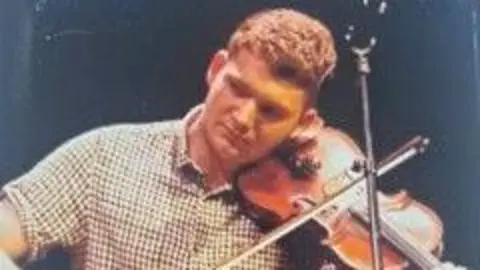 A man in a checked shirt plays the fiddle