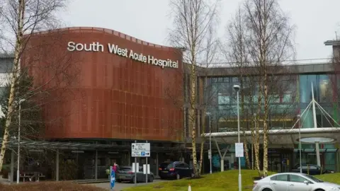 The outside of South West Acute Hospital which features a building with a brown cover attached to a glass-panelled building.  