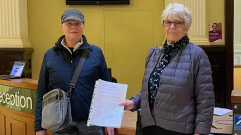 Better Together A photograph of two campaigners stood next to one another at the reception of the council's headquarters in Matlock. The lady on the right is holding the petition in her hand 