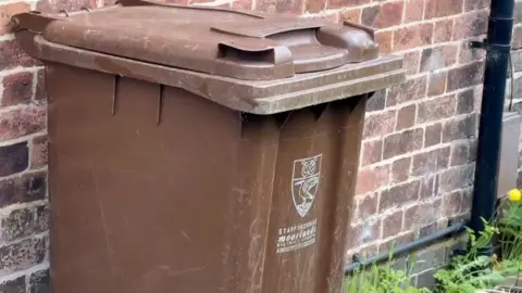 A brown garden waste bin with the Staffordshire Moorlands logo and crest on. The bin is closed.