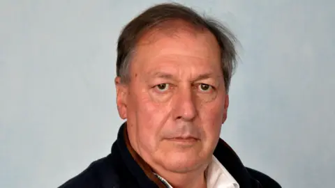 Shropshire Council Man wearing blue fleece and white shite posing for a photo in a professional studio environment with a grey background behind him