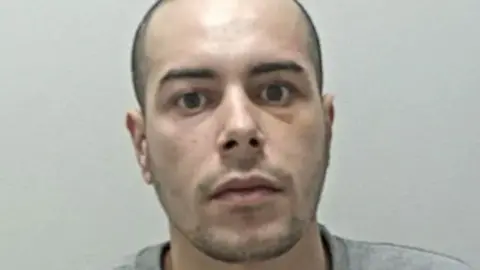 Mohammed Alshafi's mugshot. He has shaved dark hair and stubble and is wearing a grey sweatshirt
