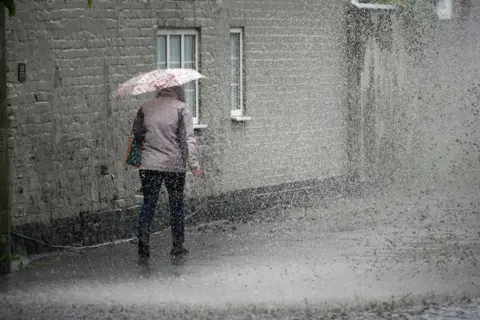 A pedestrian negotiates a partially flooded footpath as heavy rain begins on May 22, 2024 in Northwich, United Kingdom. 