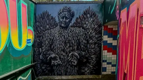 Hertfordshire County Council An image of an outdoor pedestrian underpass decorated with vibrant street art. There is lettering on the walls inspired by local children.