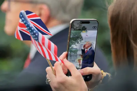 Reuters Trump is seen saluting in front of the White House on a phone as someone takes a photo holding a miniature British and American flag.