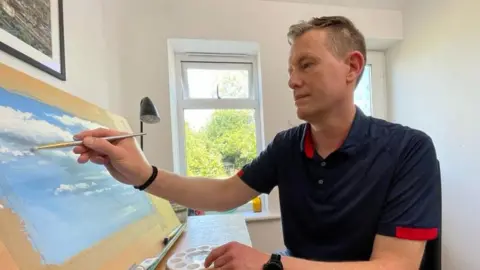 Shaun Whitmore/BBC Matthew Emeny painting a blue sky with white clouds