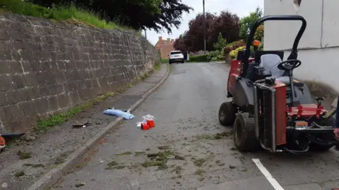 HSE Ride-on lawnmower in the road next to a wall and grass it had been mowing
