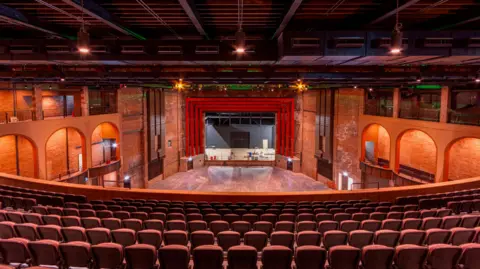 View from behind red seats inside the theatre with stage in view