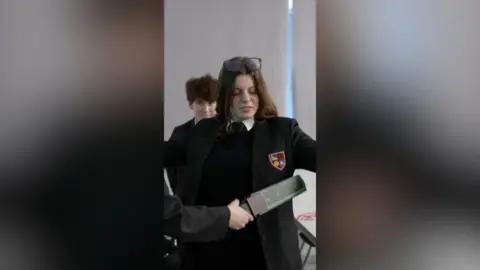 A girl in a school blazer being checked with a metal detector