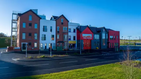 NIFRS Training warehouse with a built in local shop and fire station beside terraced buildings 