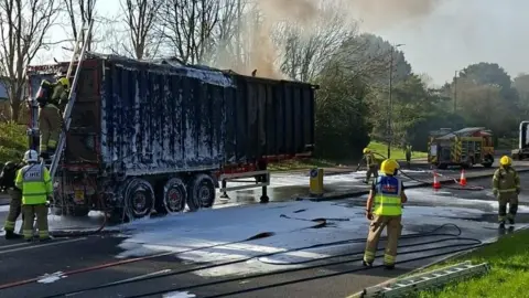 Lorry trailer with metal container on it covered in foam after being on fire.