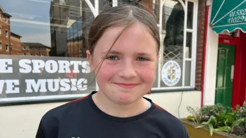BBC/Nicola Haseler Caia with long hair tied back, wearing a black top