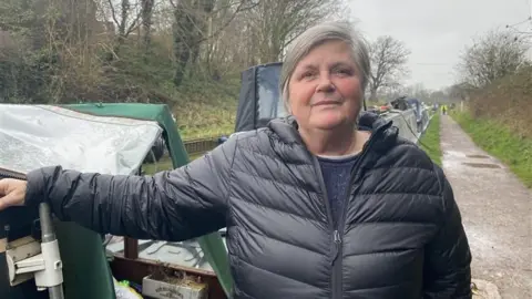 A woman in a black coat with her hand on a green narrowboat
