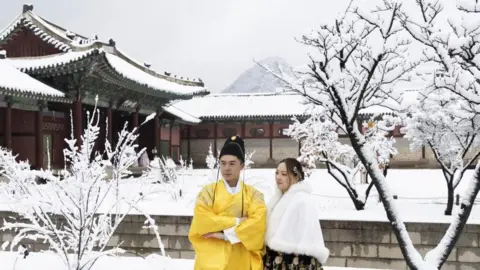 EPA-EFE/REX/Shutterstock Thai tourists wearing Korean traditional Hanbok dresses take pictures amid snowfall at the Gyeongbokgung Palace in Seoul, South Korea, 27 November 2024.