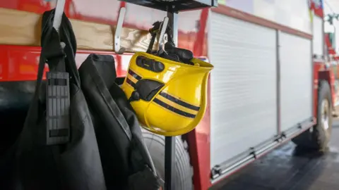 A firefighter's yellow helmet has been hung up on the side of a fire engine. 