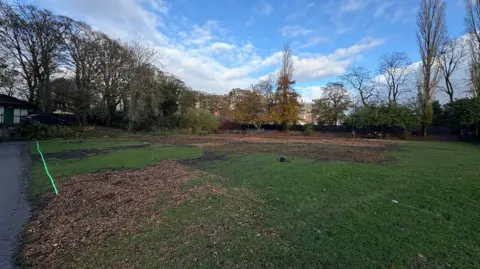 Local Democracy Reporting Service The section of the park where the maze previously stood, but this time from a different angle. The grass in the foreground is green, but where the maze stood now consists of low cut brown grass. Trees and various greens and browns are also visible around the edge of the site.