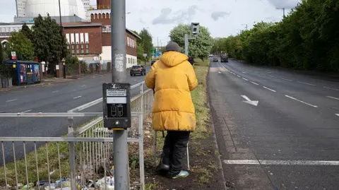 Getty Images Homeless man on crutches stands beside a main road waiting for cars to pull up at the lights.