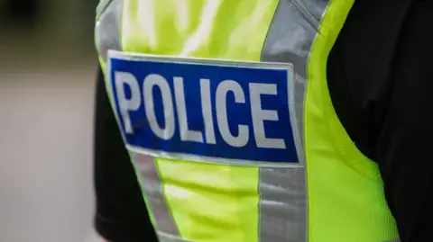 The back view of a British police vest. It is bright yellow and has silver relfective strips on either side.