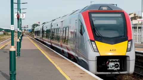 Greater Anglia A Greater Anglia train drawing into a station. The platform is in the open and has a number of lamp posts running up the middle of it. 