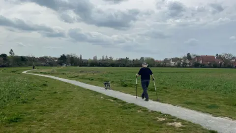 BBC/Owen Sennitt A woman with a dog walks across a path through a field towards the village of Gillingham