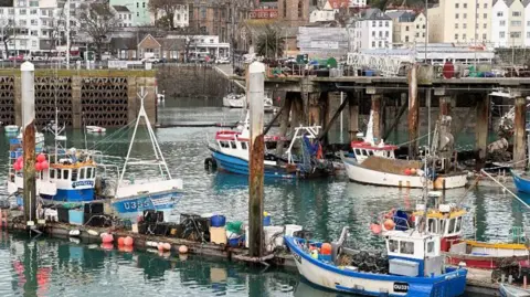 Fish Quay St Peter Port is filled with small fishing boats moored at pontoons in the harbour. Houses are close to the the harbourside.